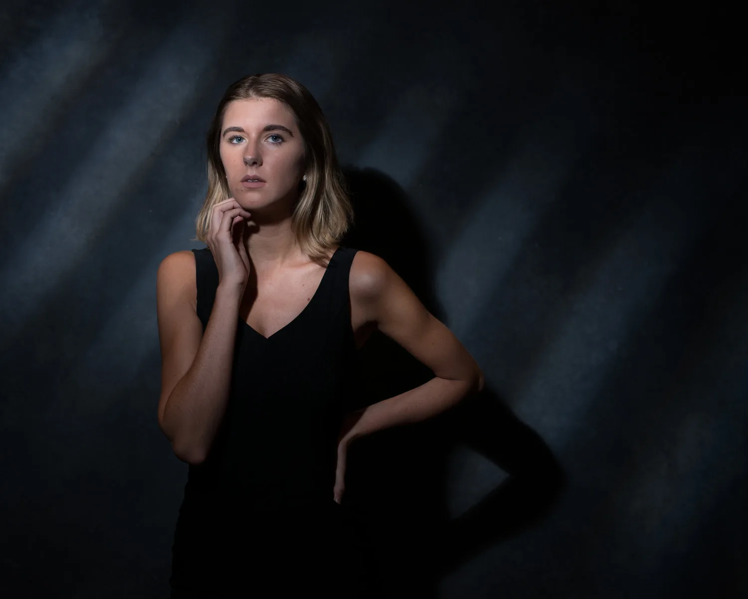 Elegant woman in black attire posing with a contemplative expression against a textured, dark background, captured by a Chester County personal branding photographer specializing in business and personal brand photoshoots.